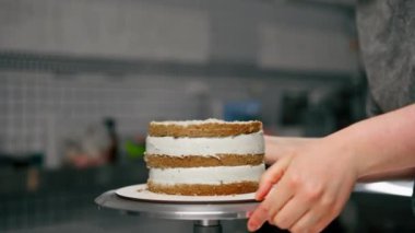 Profesyonel bir mutfakta kadın bir fırıncıyı kapamak pasta torbasından kremayı sünger kekine koyar.