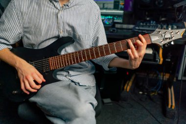 Kayıt odasındaki teçhizatta müzik çalan yakışıklı genç adam elektro gitar çalıyor ve teller doğru notayı seçiyor.