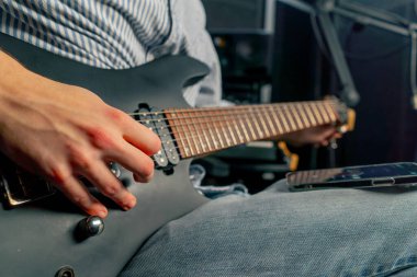 Kayıt odasının teçhizatına yaklaşın. Müziğin sesi. Yakışıklı bir genç gitarı akort ediyor.