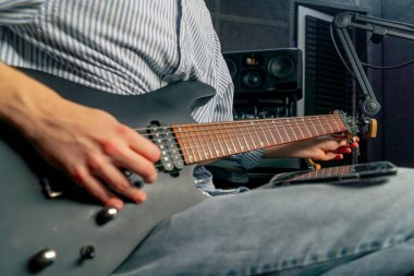 Kayıt odasının teçhizatına yaklaşın. Müziğin sesi. Yakışıklı bir genç gitarı akort ediyor.