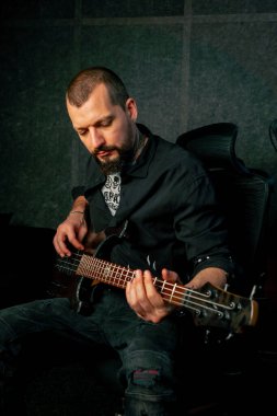 Bir kayıt odasının ekipmanında sakallı ve dövmeli yakışıklı bir adam elektro gitar çalıyor ve doğru notayı seçiyor.