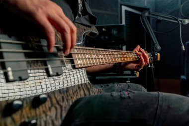 Kayıt odasının teçhizatına yakın sakallı ve dövmeli yakışıklı bir adam elektro gitar çalıyor ve doğru notayı seçiyor.