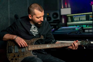 Bir kayıt odasının ekipmanında sakallı ve dövmeli yakışıklı bir adam elektro gitar çalıyor ve doğru notayı seçiyor.