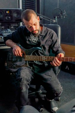 Bir kayıt odasının ekipmanında sakallı ve dövmeli yakışıklı bir adam elektro gitar çalıyor ve doğru notayı seçiyor.