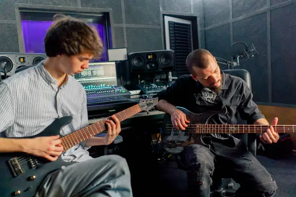 stock image in the equipment of the recording room a handsome man with a beard and tattoos and his young friend play the guitar in pairs and act out a song