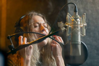 Bir kayıt stüdyosunda, temiz bir kayıt odasında, kulaklıklı güzel bir kıvırcık kız mikrofona şarkı söylüyor.