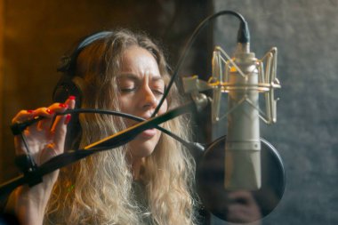 Bir kayıt stüdyosunda, temiz bir kayıt odasında, kulaklıklı güzel bir kıvırcık kız mikrofona şarkı söylüyor.