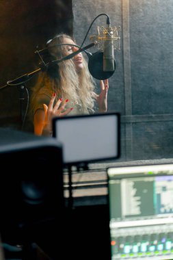 Bir kayıt stüdyosunda, temiz bir kayıt odasında, kulaklıklı güzel bir kıvırcık kız mikrofona şarkı söylüyor.