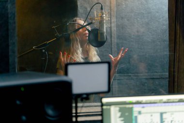 Bir kayıt stüdyosunda, temiz bir kayıt odasında, kulaklıklı güzel bir kıvırcık kız mikrofona şarkı söylüyor.