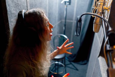 Bir kayıt stüdyosunda, temiz bir kayıt odasında, kulaklıklı güzel bir kıvırcık kız mikrofona şarkı söylüyor.