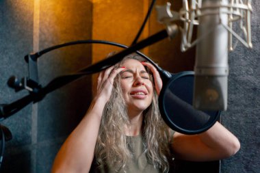 Bir kayıt stüdyosunda, temiz bir kayıt odasında, kulaklıklı güzel bir kıvırcık kız bir mikrofona şarkı söylüyor.