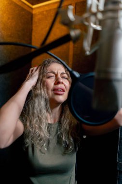 Bir kayıt stüdyosunda, temiz bir kayıt odasında, kulaklıklı güzel bir kıvırcık kız bir mikrofona şarkı söylüyor.