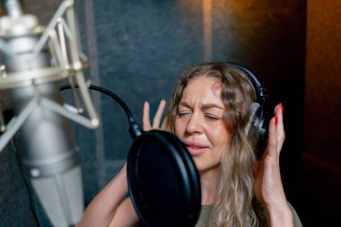 Bir kayıt stüdyosunda, temiz bir kayıt odasında, kulaklıklı güzel bir kıvırcık kız bir mikrofona şarkı söylüyor.