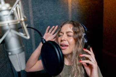 Bir kayıt stüdyosunda, temiz bir kayıt odasında, kulaklıklı güzel bir kıvırcık kız bir mikrofona şarkı söylüyor.