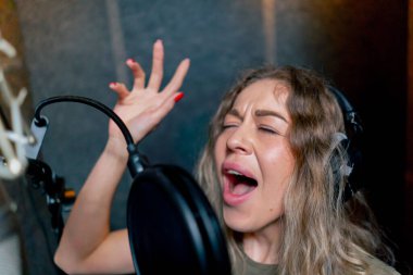 Bir kayıt stüdyosunda, temiz bir kayıt odasında, kulaklıklı güzel bir kıvırcık kız bir mikrofona şarkı söylüyor.