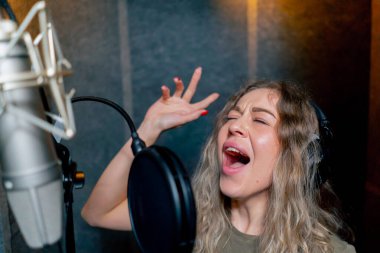 Bir kayıt stüdyosunda, temiz bir kayıt odasında, kulaklıklı güzel bir kıvırcık kız bir mikrofona şarkı söylüyor.