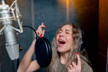 Bir kayıt stüdyosunda, temiz bir kayıt odasında, kulaklıklı güzel bir kıvırcık kız bir mikrofona şarkı söylüyor.