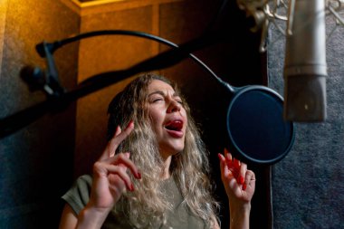 Bir kayıt stüdyosunda, temiz bir kayıt odasında, kulaklıklı güzel bir kıvırcık kız bir mikrofona şarkı söylüyor.