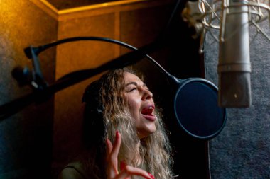 Bir kayıt stüdyosunda, temiz bir kayıt odasında, kulaklıklı güzel bir kıvırcık kız bir mikrofona şarkı söylüyor.