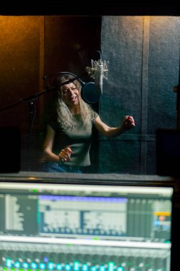 Bir kayıt stüdyosunda, temiz bir kayıt odasında kulaklıklı güzel bir kız mikrofona şarkı söylüyor. Şarkı bir monitörde kaydediliyor.