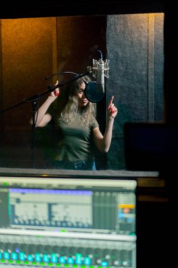 Bir kayıt stüdyosunda, temiz bir kayıt odasında kulaklıklı güzel bir kız mikrofona şarkı söylüyor. Şarkı bir monitörde kaydediliyor.