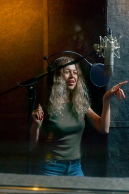 Bir kayıt stüdyosunda, temiz bir kayıt odasında, kulaklıklı güzel bir kıvırcık kız bir mikrofona şarkı söylüyor.