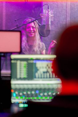 Bir kayıt stüdyosunda, temiz bir kayıt odasında kulaklıklı güzel bir kız mikrofona şarkı söylüyor. Şarkı bir monitörde kaydediliyor.