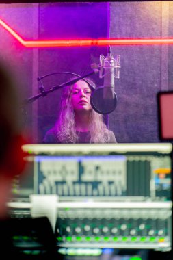 Bir kayıt stüdyosunda, temiz bir kayıt odasında kulaklıklı güzel bir kız mikrofona şarkı söylüyor. Şarkı bir monitörde kaydediliyor.