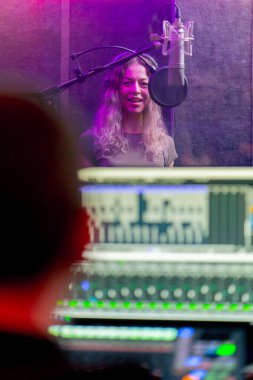Bir kayıt stüdyosunda, temiz bir kayıt odasında kulaklıklı güzel bir kız mikrofona şarkı söylüyor. Şarkı bir monitörde kaydediliyor.