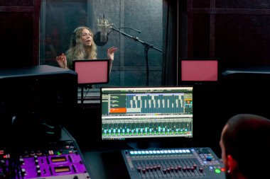 Bir kayıt stüdyosunda, temiz bir kayıt odasında kulaklıklı güzel bir kız mikrofona şarkı söylüyor. Şarkı bir monitörde kaydediliyor.