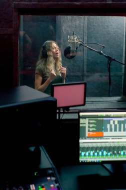 Bir kayıt stüdyosunda, temiz bir kayıt odasında kulaklıklı güzel bir kız mikrofona şarkı söylüyor. Şarkı bir monitörde kaydediliyor.