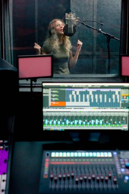Bir kayıt stüdyosunda, temiz bir kayıt odasında kulaklıklı güzel bir kız mikrofona şarkı söylüyor. Şarkı bir monitörde kaydediliyor.