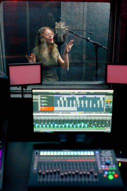 Bir kayıt stüdyosunda, temiz bir kayıt odasında kulaklıklı güzel bir kız mikrofona şarkı söylüyor. Şarkı bir monitörde kaydediliyor.