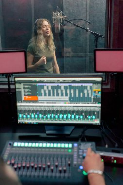 Bir kayıt stüdyosunda, temiz bir kayıt odasında kulaklıklı güzel bir kız mikrofona şarkı söylüyor. Şarkı bir monitörde kaydediliyor.