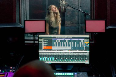 Bir kayıt stüdyosunda, temiz bir kayıt odasında kulaklıklı güzel bir kız mikrofona şarkı söylüyor. Şarkı bir monitörde kaydediliyor.