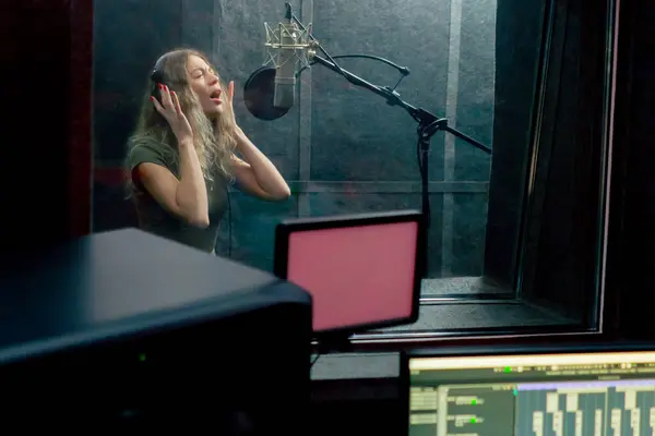 stock image in a recording studio in a clean sound recording room beautiful girl with headphones sings into a microphone the song is recorded on a monitor