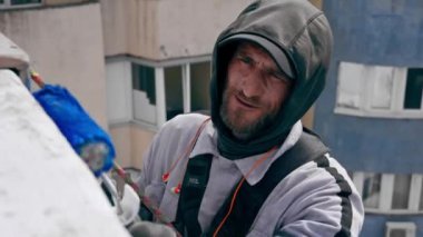 Çok renkli parlak evlerin arka planında, yüksek binaların çatısına yakın bir yerde, güvenlik ağı üzerine asılmış bir ressam duvarı maviye boyar.