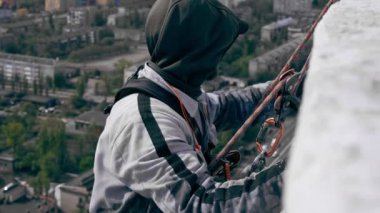 Çok renkli parlak evlerin arka planında, yüksek binaların çatısına yakın bir yerde, güvenlik ağı üzerine asılmış bir ressam duvarı maviye boyar.