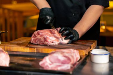 Merkezi salondaki bir kaburga barında bir restoranda siyah eldivenli bir şef büyük bir parça domuz etini kare parçalara ayırıyor.