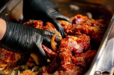 Merkezi salondaki bir kaburga barında bir restoranda siyah eldivenli bir şef salamurada et yoğuruyor.