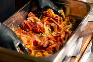 Merkezi salondaki bir kaburga barında bir restoranda siyah eldivenli bir şef salamurada et yoğuruyor.