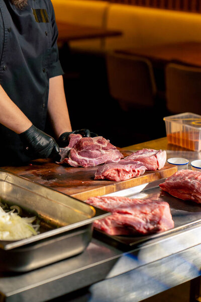 in a restaurant in a rib bar in the central hall, a chef in black gloves cuts a large piece of pork meat into square pieces
