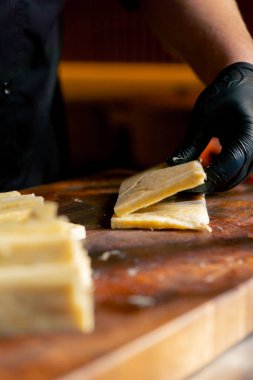 Merkezdeki kaburga barında yakın bir restoranda ahşap bir tahtanın üzerinde siyah eldivenli bir şef peyniri peynir çubuğu yapmak için şeritlere ayırıyor.