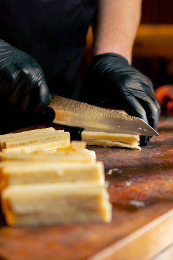 Merkezdeki kaburga barında yakın bir restoranda ahşap bir tahtanın üzerinde siyah eldivenli bir şef peyniri peynir çubuğu yapmak için şeritlere ayırıyor.