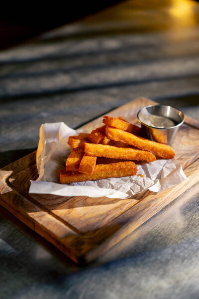 Закрыть в ресторане на железном столе готовое блюдо из сырных палочек с соусом на деревянной доске с бумагой, подпирающей хрустящую корочку