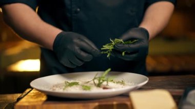 Merkezi salondaki bir kaburga barında bir restoranda siyah eldivenli bir şef koyu mavi bir tabağa salata kompozisyonu koyar.
