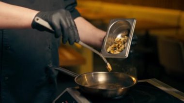 Merkezi salondaki pirzola barında, sarı ışıklı bir restoranda, siyah eldivenli bir şef, ısıtılmış tavada midye kızartıyor.