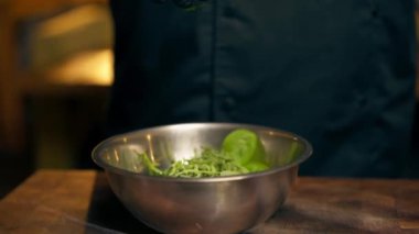 Merkezdeki bir kaburga barında, sarı ışıklı bir restoranda, siyah eldivenli bir şef, tabağa koymak için marul yaprakları hazırlar.