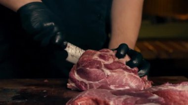 Merkezi salondaki bir kaburga barında bir restoranda siyah eldivenli bir şef büyük bir parça domuz etini kare parçalara ayırıyor.