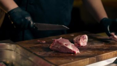 Merkezi salondaki bir kaburga barında bir restoranda siyah eldivenli bir şef büyük bir parça domuz etini kare parçalara ayırıyor.